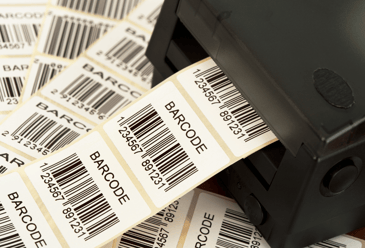 A thermal printer in the middle of printing a sheet of barcode labels and surrounded by numerous prior print jobs showcasing its speed and efficiency.